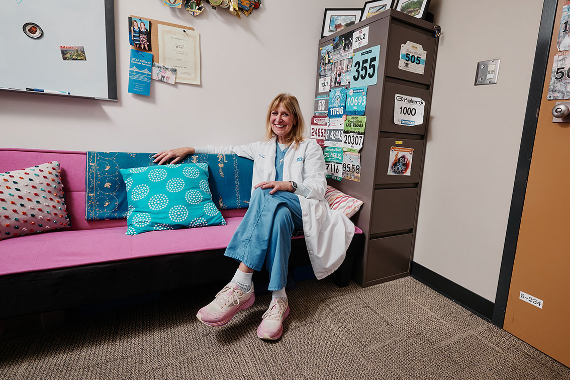 Barbara Bates-Jensen in lab outfit sitting on pink couch in her office. Running medals are hung on the walls.